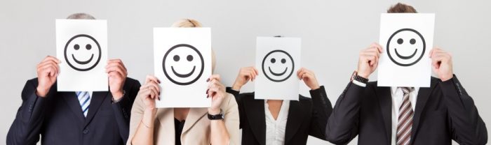 4 office workers holding a happy smiley face piece of paper in front of their faces