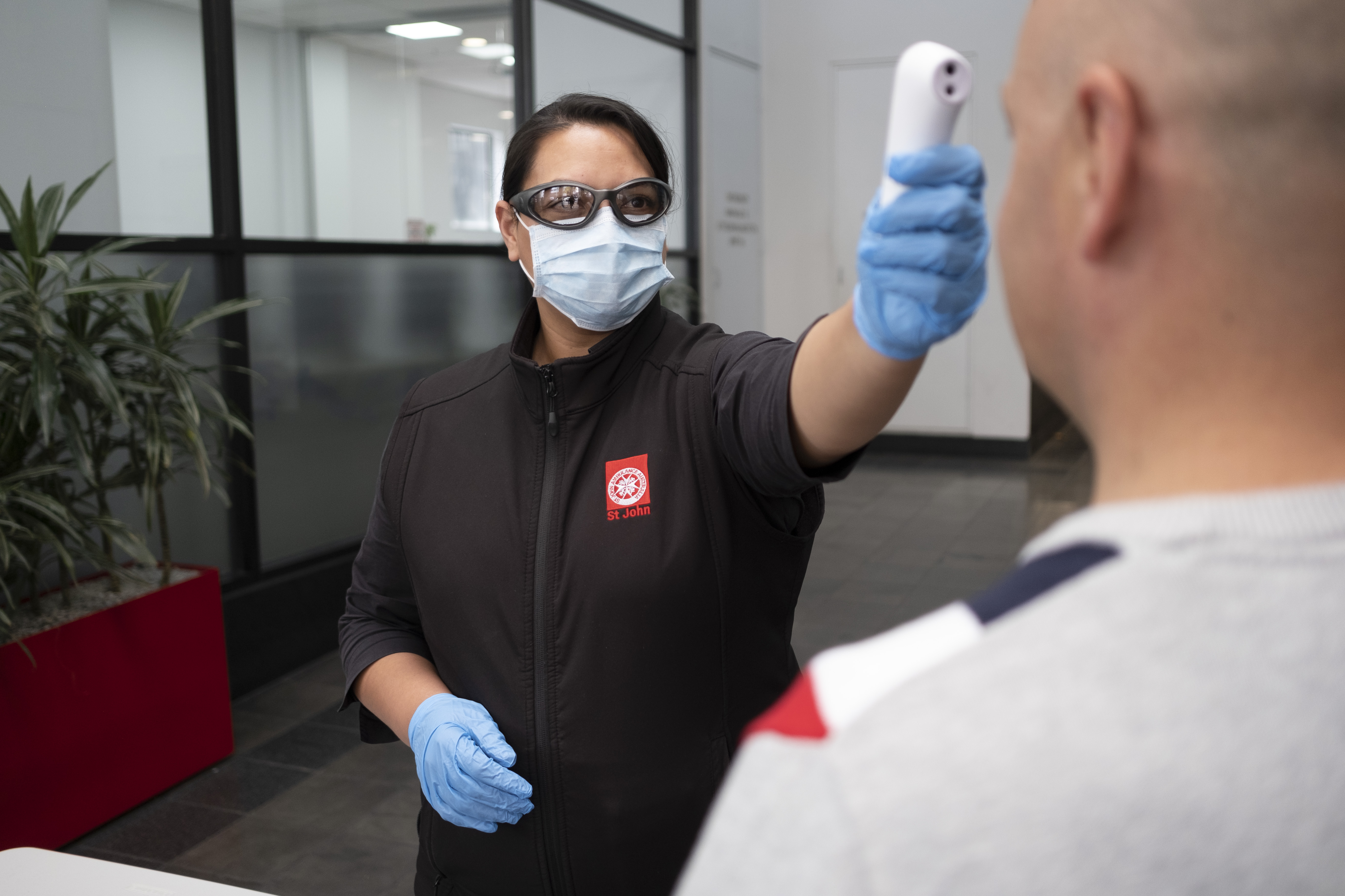 St john trainer dressed in PPE temperature screening man