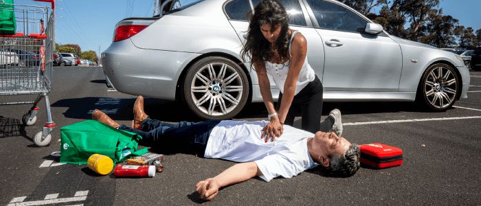 woman performing CPR on unconscious man in shopping centre car park